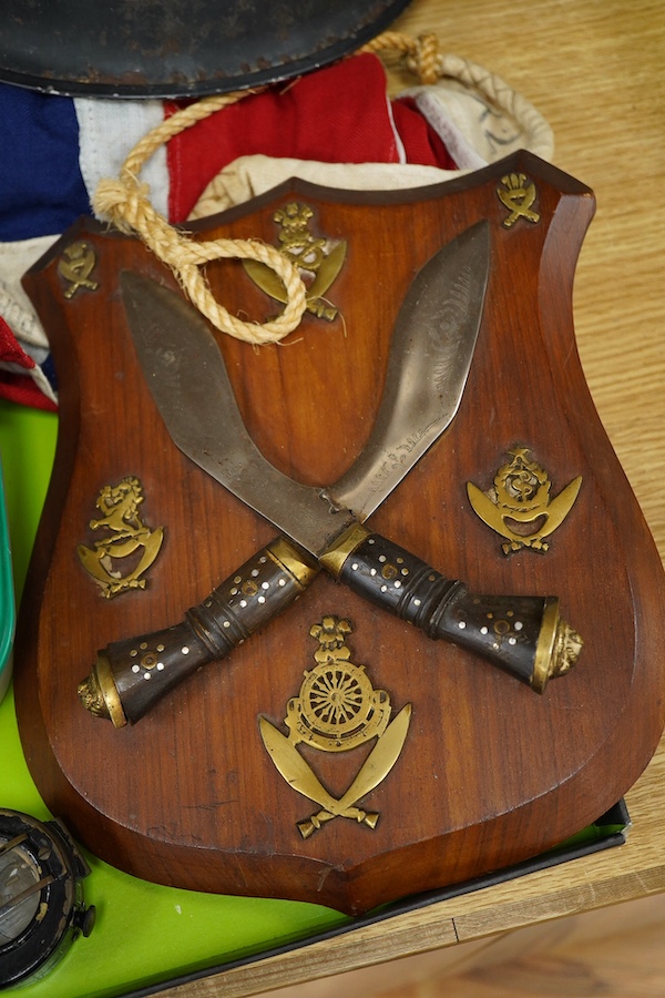 A collection of military items, including a U.S. Army helmet, an M42 helmet, a WWII British Home Front helmet, a Union flag 96cm x 60cm, a compass, a Kukri display shield, and a box of military cap badges, buttons, etc.